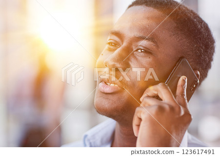 shot of confident young Afro-American man walking through lobby of busy office building, talking on smartphone and smiling 123617491