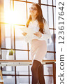 Beautiful confident young busines woman with black hair in a modern office standing near the table with a folder in her hand 123617642