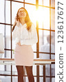 Smiling businesswoman on the phone standing at full height and looking at camera in an office 123617677
