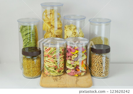Variety of multi-colored pasta and and other groceries in glass containers. Types of uncooked pasta, chickpeas, rice and bulgur. Storing different food at home. 123620242