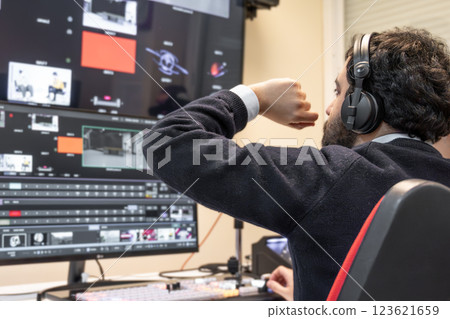 A television director in a broadcast control room, actively guiding a live production. Surrounded by 123621659