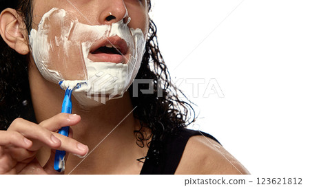 Close-up cropped image of young man mid-shave, razor gliding through thick foam, against white studio background. 123621812