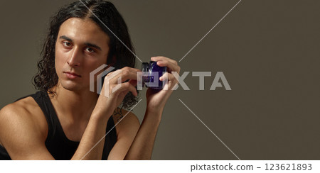 Handsome young guy with well-kept skin and curly hair, holding jar with styling gel against studio background 123621893