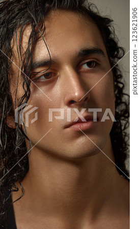 Close-up of handsome young guy with glowing skin and wet curls gazing into distance against neutral background. 123621906
