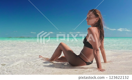 Woman is enjoying the sun and the turquoise water of the indian ocean while sitting on a white sand beach in the maldives 123622132