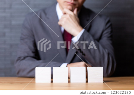 四塊白色木塊和一位身著西裝、憂心忡忡的中年男性商人 123622180