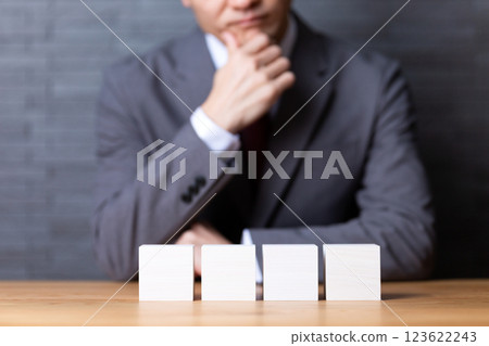 四塊白色木塊和一位身著西裝、憂心忡忡的中年男性商人 123622243