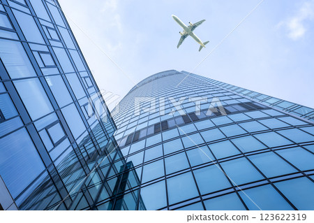 Bottom up view of modern glass skyscraper and passenger airplane flying over it Bottom up view of modern glass skyscraper and passenger airplane flying over it 123622319