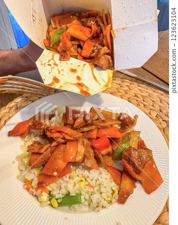 Takeout food being poured onto a plate of rice, vegetables and meat in sauce. High quality photo 123623104