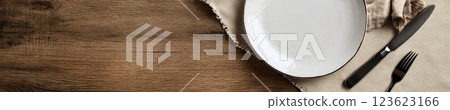 White empty plate with silver cutlery on a rustic wooden table, beige napkin in a diamond layout. Natural lighting and warm wood tones create a cozy, inviting atmosphere with wide copyspace. White empty plate with silver cutlery on a rustic wooden table, beige napkin in a diamond layout. Natural lighting and warm wood tones create a cozy, inviting atmosphere with wide copyspace. 123623166