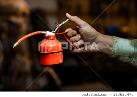 Close-up of Hand Holding Red Oil Can in Mechanical Workshop Environment Close-up of Hand Holding Red Oil Can in Mechanical Workshop Environment 123623473