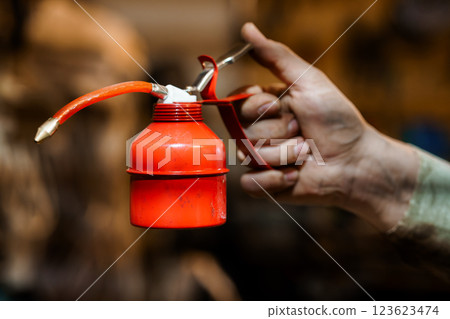 Vintage Red Oil Can Held by a Worker in a Workshop Setting 123623474
