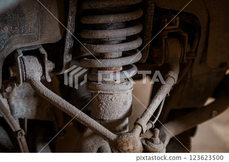 Close-up View of Dusty and Rusty Suspension System of Vehicle Showing Shock Absorber, Coil Spring, and Control Arms 123623500