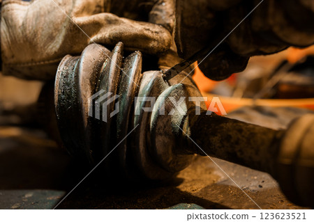 Close-up of mechanic hands repairing and inspecting automotive CV axle shaft joint boot in workshop conditions Close-up of mechanic hands repairing and inspecting automotive CV axle shaft joint boot in workshop conditions 123623521