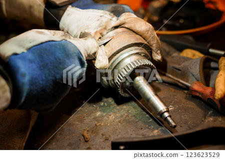 Close-Up of Worker Hands Wearing Gloves Repairing Mechanical Part with Tools in Workshop Setting 123623529