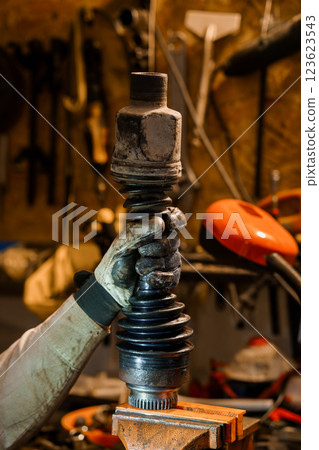Detailed Close-Up of a Mechanic's Hand Holding a Car CV Joint in a Workshop Setting 123623543