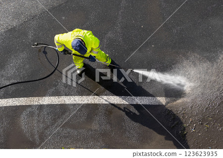 Road worker cleaning asphalt with high pressure water jet 123623935