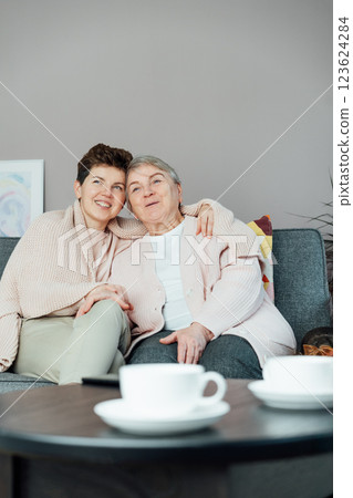 Neutral gender woman hugging her senior mom or grandma and watching TV, sharing tender moment together. Parenting love, care and generations unity concept. Mothers day. Happy family enjoying weekend. 123624284