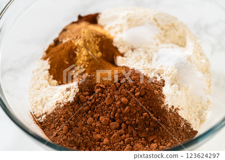 Mixing dry ingredients for Chocolate Gingerbread Cookie Dough, including flour, cocoa powder, cinnamon, ground ginger, and cloves in a glass bowl. The ingredients are layered and ready to be combined 123624297