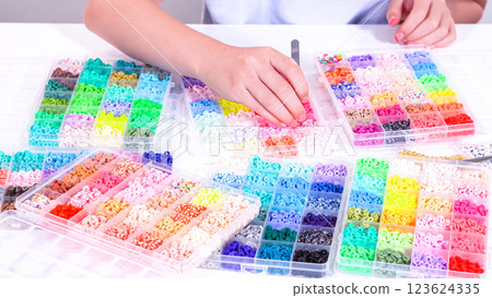 Delicate fingers of a young girl navigate through a treasure trove of bright, multicolored beads, each compartment revealing a new hue to choose from. 123624335