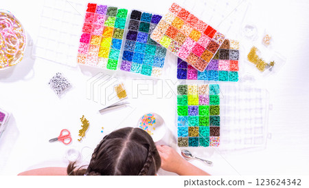 Flat lay. Delicate fingers of a young girl navigate through a treasure trove of bright, multicolored beads, each compartment revealing a new hue to choose from. 123624342