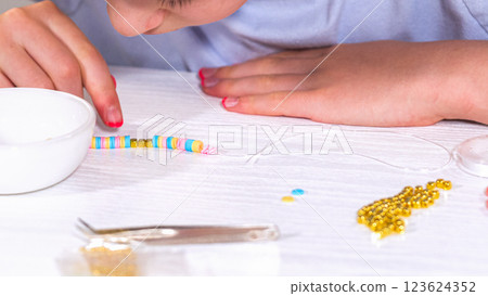 Delicate fingers of a young girl navigate through a treasure trove of bright, multicolored beads, each compartment revealing a new hue to choose from. She's immersed in the joyful task of stringing Delicate fingers of a young girl navigate through a treasure trove of bright, multicolored beads, each compartment revealing a new hue to choose from. She's immersed in the joyful task of stringing 123624352