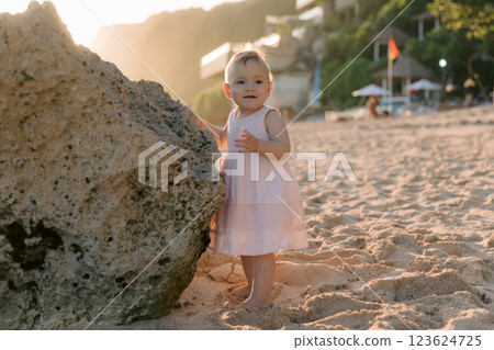 Beautiful baby in outdoor with sunlight. Child in pink dress staying on sunset beach. 123624725