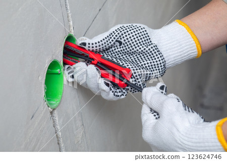 The electrician removes the protective sheath from the wire. 123624746