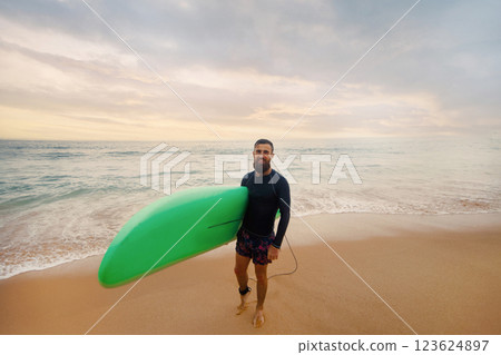 Young  bearded man with surfboard standing near a beach. Man with surfing board outdoors on a summer day 123624897