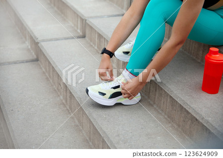 Fitness Enthusiast Ties Shoelaces While Preparing for Workout on Outdoor Stairs in Bright Athletic Gear 123624909