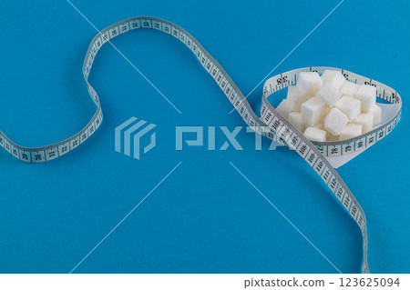Sugar cubes in a bowl with a measuring tape on a blue background Sugar cubes in a bowl with a measuring tape on a blue background 123625094