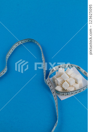 Sugar cubes and measuring tape on a blue background showcasing health awareness Sugar cubes and measuring tape on a blue background showcasing health awareness 123625095