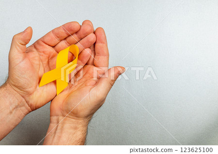 Support for cancer awareness with a symbolic yellow ribbon in hands Support for cancer awareness with a symbolic yellow ribbon in hands 123625100