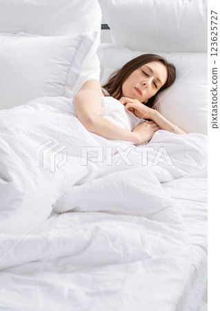 young woman sleeping on bed with white linen and air pillows. Correct regime and good sleep for female cycle 123625727