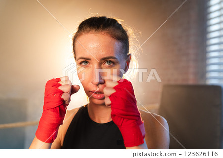 Women self defense girl power. Strong woman fighter punching with red boxing wraps sports protective bandages. Girl punching training punches looking concentrated straight. Fit body workout Women self defense girl power. Strong woman fighter punching with red boxing wraps sports protective bandages. Girl punching training punches looking concentrated straight. Fit body workout 123626116