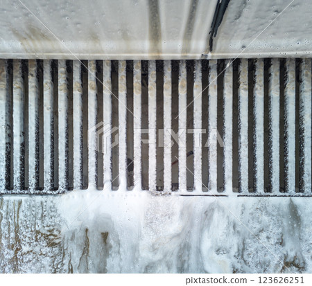 Soap sud waste flows to floor drain grid in car washing garage, close-up. Soap sud waste flows to floor drain grid in car washing garage, close-up. 123626251