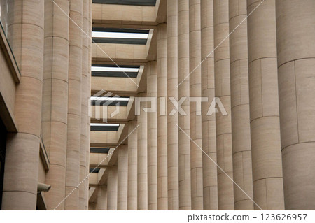 Modern Architectural Columns showcasing Geometric Pattern. Smooth, beigecolored stone pillars form rhythmic and repetitive design. Overhead beams add interplay light and shadow, structure's symmetry. 123626957