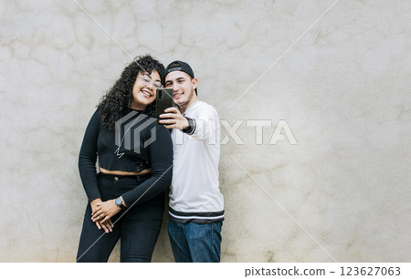 Young couple taking a selfie near a wall with copy space, Young friends taking a selfie leaning against a wall, Young happy couple taking a selfie leaning against a wall Young couple taking a selfie near a wall with copy space, Young friends taking a selfie leaning against a wall, Young happy couple taking a selfie leaning against a wall 123627063