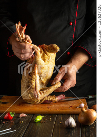 A chef skillfully handles a whole duck, preparing it for cooking on a wooden cutting board in a kitchen. Fresh ingredients like garlic and onion are nearby A chef skillfully handles a whole duck, preparing it for cooking on a wooden cutting board in a kitchen. Fresh ingredients like garlic and onion are nearby 123627326