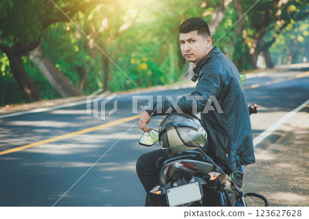 Latin motorcyclist sitting on his motorbike near an asphalt road. Portrait of biker in jacket sitting on his motorcycle at the side of the road 123627628