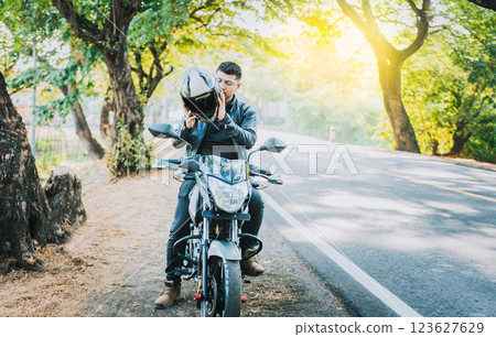 Close-up of motorcyclist man putting on safety helmet. Biker motorcycle putting on safety helmet near of asphalt road. Biker motorcycle safety concept Close-up of motorcyclist man putting on safety helmet. Biker motorcycle putting on safety helmet near of asphalt road. Biker motorcycle safety concept 123627629