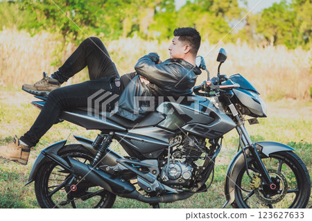 Biker man lying down on his motorbike outdoors. Motorcyclist in jacket lying on his motorcycle in the countryside Biker man lying down on his motorbike outdoors. Motorcyclist in jacket lying on his motorcycle in the countryside 123627633