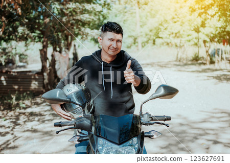Biker on his motorbike holding safety helmet with thumb up. Concept of Smiling motorcycle cyclist holding safety helmet, Biker man giving thumb up while holding safety helmet 123627691