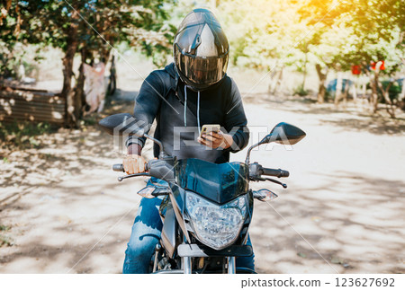Man on motorbike texting while driving. Motorcyclist on motorcycle using cell phone outdoors. Concept of distracted motorcyclist with cell phone. Man on motorbike texting while driving. Motorcyclist on motorcycle using cell phone outdoors. Concept of distracted motorcyclist with cell phone. 123627692