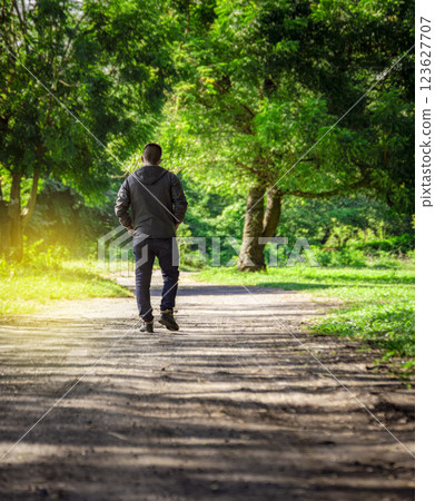 Man walking down a desolate road, man walking backwards on a road surrounded by vegetation Man walking down a desolate road, man walking backwards on a road surrounded by vegetation 123627707
