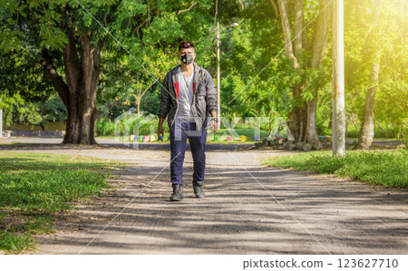 Man walking in the street with face mask on, man walking head-on in the street with face mask, young man with mask walking down the street Man walking in the street with face mask on, man walking head-on in the street with face mask, young man with mask walking down the street 123627710