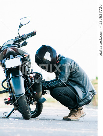 Man checking his motorcycle on the road. Motocyclist fixing the motorcycle on the road, Biker repairing motorcycle on the road 123627726