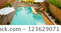 Modern swimming pool with turquoise water, wooden deck, umbrellas, and lounge chairs in a tranquil backyard 123629071
