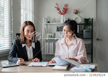 Two women engaged in a business meeting, discussing documents in a modern office environment with natural light. 123629224