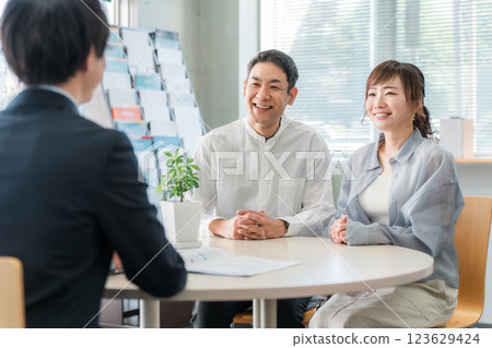 A couple listening to a conversation in a showroom/business negotiation space and a businessman serving them A couple listening to a conversation in a showroom/business negotiation space and a businessman serving them 123629424